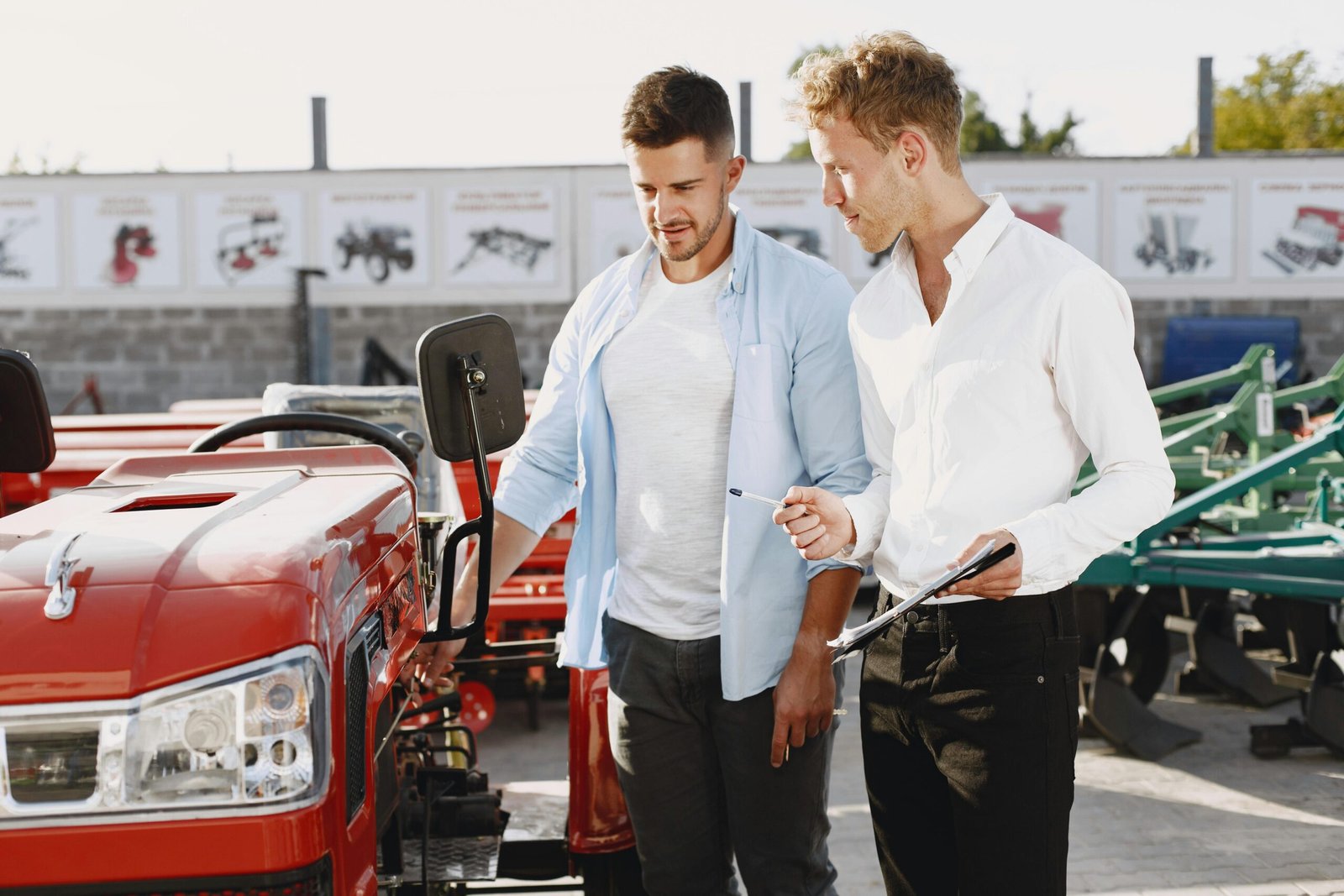 Two men having a discussion about a red tractor in an outdoor setting, possibly negotiating a deal.